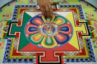 Bir Tibetli keşiş parmağını renkli kum mandalını karıştırmak için kullanır ve onu bir yığın içine süpürür.. 
