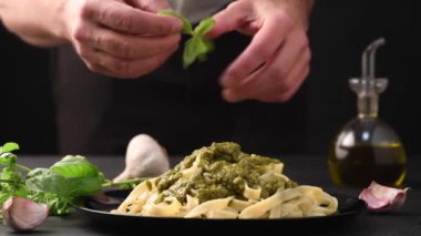 Şef fesleğen yaprağıyla süslüyor. Genovese pesto soslu makarna tabağı siyah masada sos malzemeleriyle.