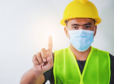 Tıbbi maskeli mühendis, seçilmiş parmak üzerine odaklanmış şeffaf ekran ekranına dokunuyor. Yapılandırma Konsepti.