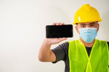 Tıbbi maskeli mühendis elinde akıllı telefon tutuyor..