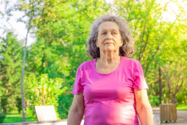 Olgun bir kadın güneşli bir günde yeşil ağaçların arka planında yürür. Ciddi bir yüzü olan yaşlı bir kadın. Depresif bir ruh hali. Psikoloji. Gururlu bir bakış. Eski nesil..