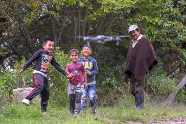 Villa de Leyva, Boyaca, Colombia - December 7, 2017: A group of local kids and a man with his usual outfit watching  with awe a drone fly in front of them.