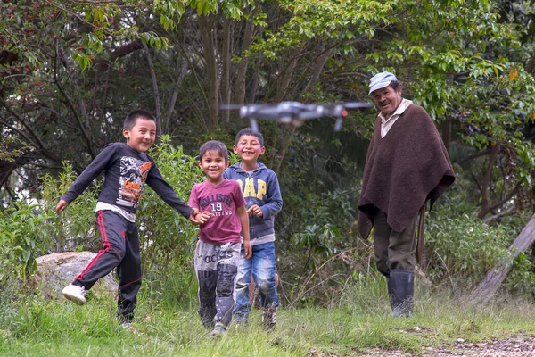 Villa de Leyva, Boyaca, Colombia - December 7, 2017: A group of local kids and a man with his usual outfit watching  with awe a drone fly in front of them.