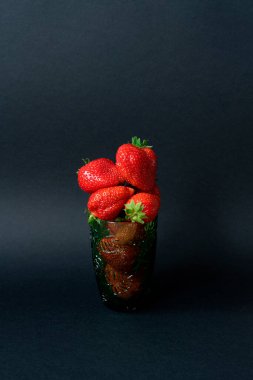 Siyah arka planda yeşil bardakta çilekler.