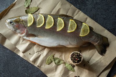 Siyah mermer zemin üzerinde limon ve baharatla dolu bir somon.