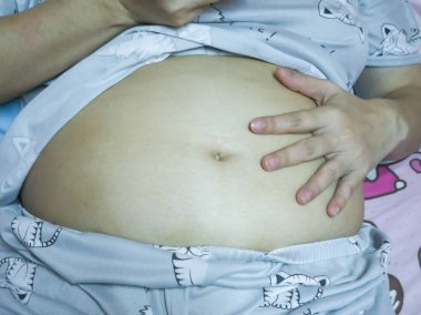 Pijama giyen Asyalı kadınlar, elleri karnına dokunuyor, hamilelik ya da obezite, Tayland.