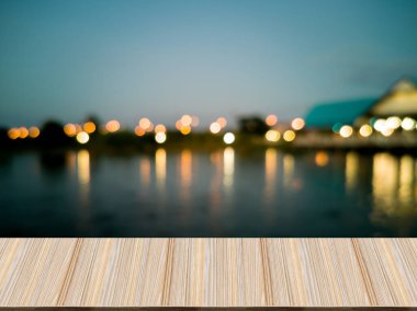 Öndeki yapay ahşap masa. Bulanık arka plan, gölcük ve sudan yansıyan ışıklarla birlikte küresel bokeh. Akşam karanlığında arkaplan resmi.
