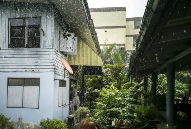Yağmur oluğu olan eski evlere, kırsal bölgelere ya da banliyölere yağmur yağar. Etrafta ağaçlar var, tropiklerin yağışlı mevsiminde, Asya.