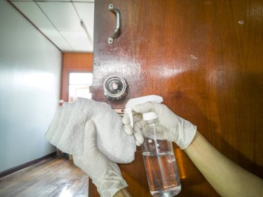 Göz hizasında, temiz paslanmaz çelik kapı tokmağı (ahşap kapı kolu), temiz bez ve alkol spreyi kullanarak, beyaz eldivenli eller.