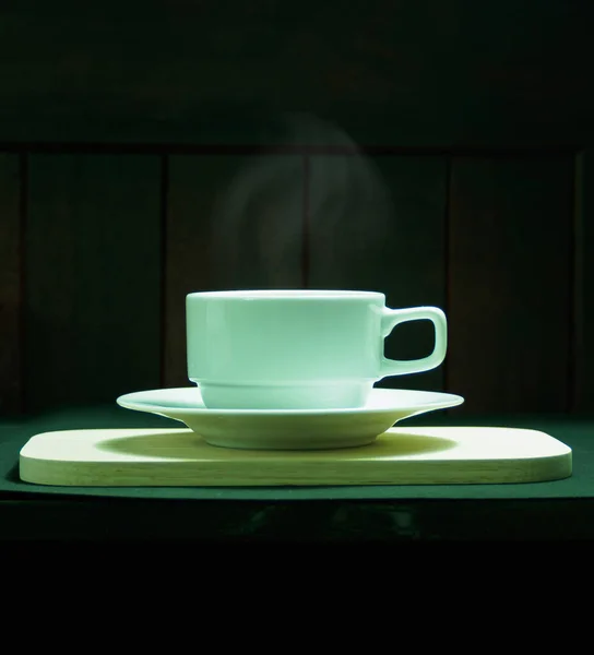 目のレベルショット 白いコーヒーカップとライターの煙とソーサー 木製のプレート 黒の背景 — ストック写真