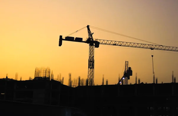 Bitmemiş binaların silueti ve büyük inşaat vinçleri, gün batımı.