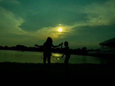 İki kızın silueti mutlu, neşeli, neşeli, mutlu, gölün önünde, gölette, parkta, akşam, gün batımında.