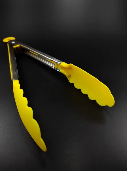 Photo Yellow Tongs Cooking Isolated Black Background Focus — Stock Photo, Image