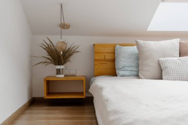 Konforlu yatak odasının yanındaki komodinin üzerinde vazo olan modern bir daire. Beyaz minimalist odada ev dekorasyonu ve ahşap mobilyalar.
