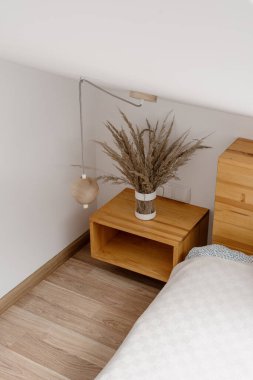 Yatak odasındaki rahat yatağın yanında ahşap komodinin dikey ve yüksek açılı görüntüsü. Çağdaş dairede konforlu oda kavramı