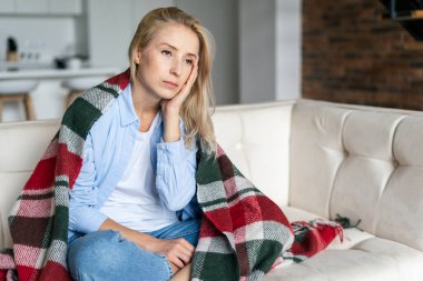 Hasta ve bitkin bir kadın alnına dokunur, baş ağrısı, kronik migren ya da depresyon, battaniyeyle kanepede oturur. Sinirli kadın stresli, yüksek ateş ve şakaklarda yüksek tansiyon hisseder.