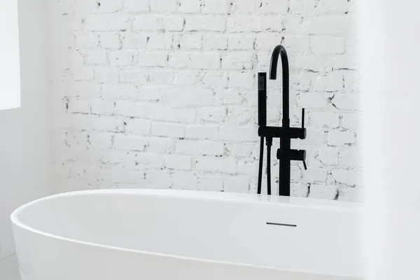 白のモダンなアパートや高級ホテルの部屋で明るいインテリアデザインのバスルーム 黒い蛇口と空のエレガントな浴槽の上に頭をシャワー付きの快適なバスルームの垂直方向のビュー 広告コンセプト — ストック写真