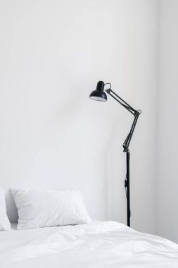Beyaz iç tasarımı olan zarif nesneler dairede. Rahat yatağın üzerinde siyah lamba olan rahat yatak odası dikey görünümü. Temiz ve doğal pamuklu yatak. Otel servis kavramı
