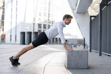 Spor için egzersiz ve fonksiyonel egzersiz kavramı. Kalas pozisyonunda duran sporcunun profil görüntüsü, kutudan şınav çekmesi, şehir dışında antrenman yapması, tam boy.