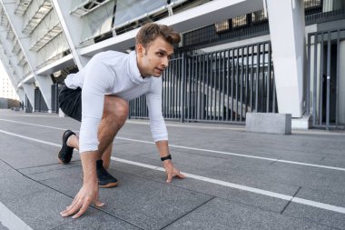 Yarışma, maraton ve sprint koşu konsepti. Başlangıç çizgisinde el ele tutuşup stadyumda koşmaya hazırlanan odaklanmış koşucunun yan görüntüsü. Adam dışarıda antrenman yapmaya hazırlanıyor.