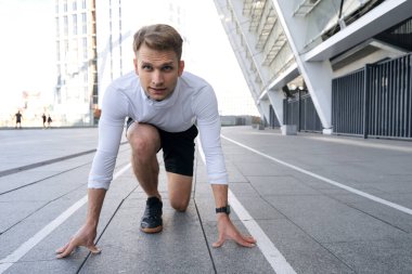 Başlangıç pozisyonunda genç bir sporcunun portre görüntüsü, el ele tutuşması, spor pistinde ısınmaya hazırlanması. Koşu antrenmanı, sokakta koşmaya hazırlanmak.