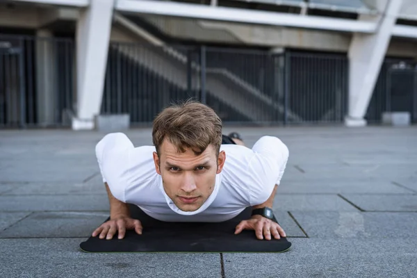 Açık havada antrenman yapan güçlü bir sporcunun portresi, yoga minderinde çalışmak, şınav çekmek ya da şınav çekmek, kameraya bakın. Spor giyim sektöründe kendine güvenen ve konsantre bir sporcu. Fiziksel aktivite kavramı
