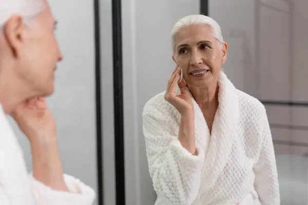 Güzel Yaşlı Bir Kadının Portresi Yüzünü Süngerle Siliyor Aynaya Bakıyor — Stok fotoğraf