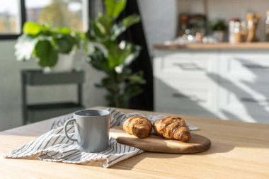 Çağdaş mutfak içinde çay ve kruvasanla rahat bir ortam. Sabah rutini. Ev yapımı pişirme konsepti. Arka planda modern beyaz mobilya ve bitkiler