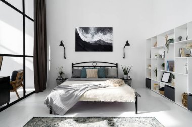 Çağdaş yatak odası iç tasarımına beyaz tonlarda tam bir bakış açısı. Duvarda asılı olan soyut resim. Dekorlu ve kitaplı modern raflar. Satılık lüks daire.