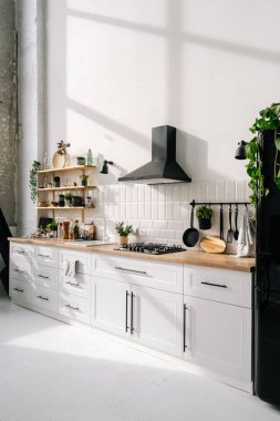 Beyaz mobilyalar, raflar, buzdolabı, kaput ve ev aletleri ve dekorasyonlarla parlak modern mutfak iç tasarımı. Tarafsız duvar ve yemek odasındaki zemin