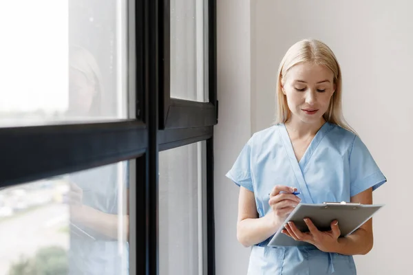 身穿蓝色制服的忙碌的护士检查病人记录 站在医院 拿着带有文件和社会保险文件的剪贴板 免费医疗合同的概念 — 图库照片