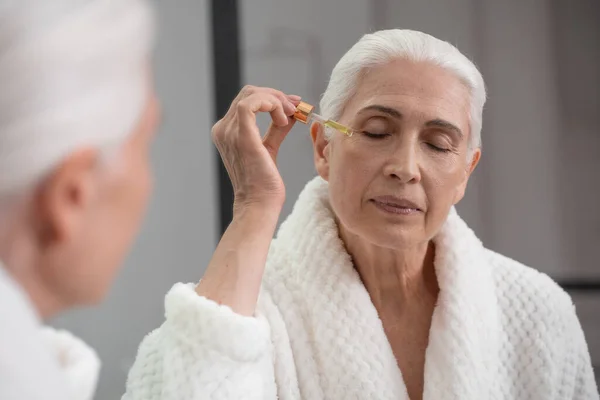 Güzel Yaşlı Bir Kadının Portresi Aynanın Karşısında Yaşlanma Karşıtı Serum — Stok fotoğraf