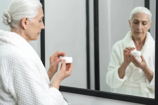 Aynanın Önünde Duran Krema Kavanozlu Yaşlı Kadın Portresi Yaşlanma Önleyici — Stok fotoğraf