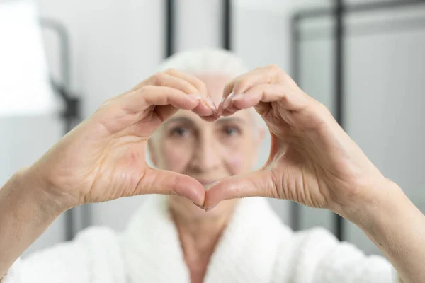 Elleriyle Kalp Sembolü Yapan Bornozlu Çekici Yaşlı Bir Kadın Kendini — Stok fotoğraf