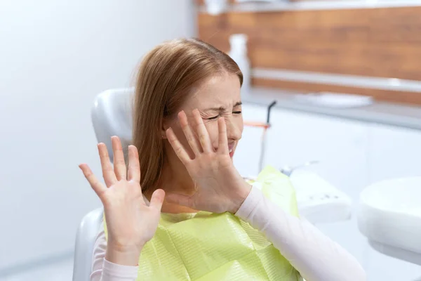 紧张的病人害怕牙齿治疗 口腔科诊所的女性恐惧症患者 做停止姿势 用手捂住脸 以避免与牙医检查 — 图库照片