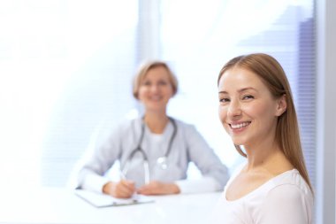 Mutlu ve sağlıklı hasta kameraya bakıyor, geniş gülümsüyor, bulanık arka planda doktorun karşısında oturuyor. Kliniği ziyaret etme, tedavi, sağlık ve sağlık kontrolü