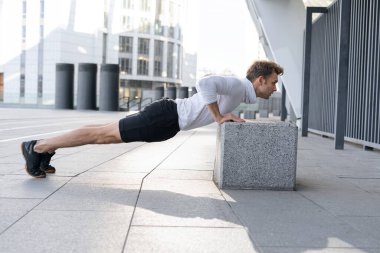 Spor antrenmanındaki genç sporcunun profil görüntüsü açık havada şınav çekerken ya da şınav çekerken, düşük kalas pozisyonunda duruyor. Yoğunlaşmış bir adam günlük antrenmandan önce vücudunu ısıtır.