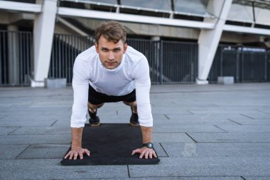 Sportif bir adamın tahta duruşunu, vücudunu dışarıda eğitmesini spor minderinde antrenman yapmasını, ıkınmasını ya da şınav çekmesini, kameraya bakmasını. Fiziksel aktivite, eğlence, yaşam tarzı konsepti
