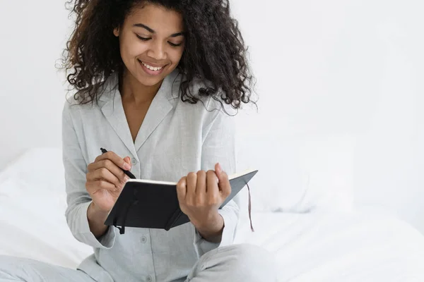 Vrolijke Donkere Vrouw Met Een Brede Glimlach Die Notities Schrijft — Stockfoto