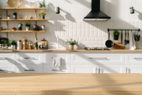 Scandinavian kitchen interior design with white furniture and diverse decorations. Wood stylish table in foreground. Household appliances. Bright dining room after repair