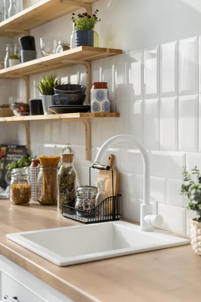 Beyaz lavabo modern mutfak içinde beyaz tonlarda. Mutfak aletleriyle ahşap raflar. Arkasında mısır gevreği olan şeffaf kavanozlar. Çağdaş daire