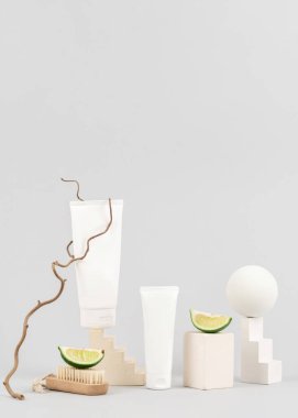 Kozmetik ürünlerini sergilemek için geometrik şekilli podyum. El ve vücut kremli beyaz tüpler. Açık gri zemin üzerinde turunçgil şampuanı ve saç kremi olan bir paket.
