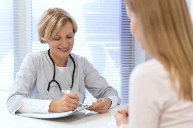 Aile doktoru hasta kayıtlarına notlar yazar, ilaç yazar, genç bir kadın için tedavi planını tartışır. Pratisyen hekim özel klinikteki sağlık sigortası sözleşmesini kontrol etti