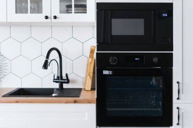 Beyaz mobilyalar ve siyah aletlerle modern İskandinav tarzı mutfak manzarası. Yemek yapmak için güzel bir yer. Satılık lüks daire.