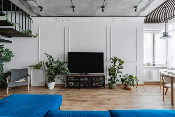 青いソファと大きなテレビ付きの広々としたロフトスタイルのアパート 居心地の良い家庭環境 装飾や植物とモダンな家のインテリアデザイン ラグジュアリー ミッション — ストック写真