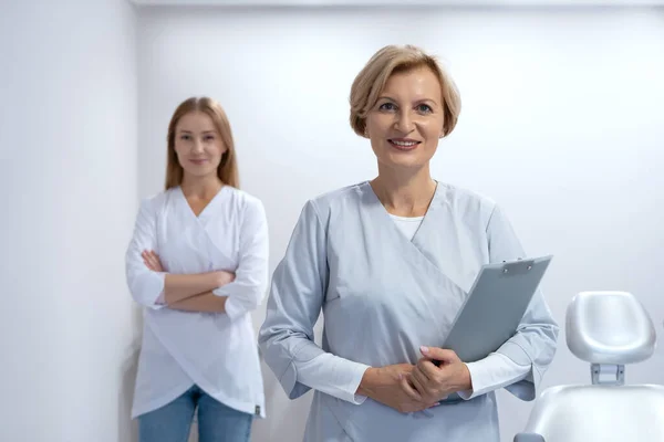 微笑的医生和她的年轻助手的画像 当代医院办公室 卫生保健概念 医疗部门 疾病预防护理 — 图库照片