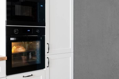 Mutfak iç tasarımında siyah fırının yan görüntüsü. Yemek pişirme süreci. Çağdaş beyaz ahşap mobilyalar. Yemek yapmak için rahat bir yer.