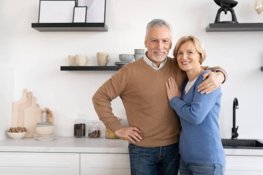 Modern, rahat bir mutfakta kameraya bakan mutlu orta yaşlı bir çiftin portresi. Mutlu bir aile. Sonsuza dek aşk konsepti. Bağlılık ve özen