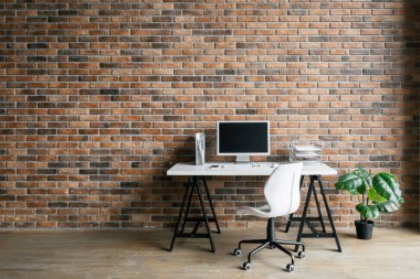 Bilgisayar beyaz masada, modern çatı katı tarzı iç tasarımı olan bir sandalye. Merkez ofis konsepti. Uzaktan kumanda. Ev rahatlığı. Rahat bir iş yeri