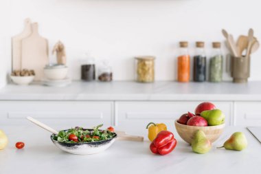 Parlak beyaz tonlu mutfakta sebze salatası yapıyorum. Sağlıklı bir yaşam tarzı. Ev rahatlığı. Masada taze meyve ve sebze var. Sağlıklı gıda konsepti